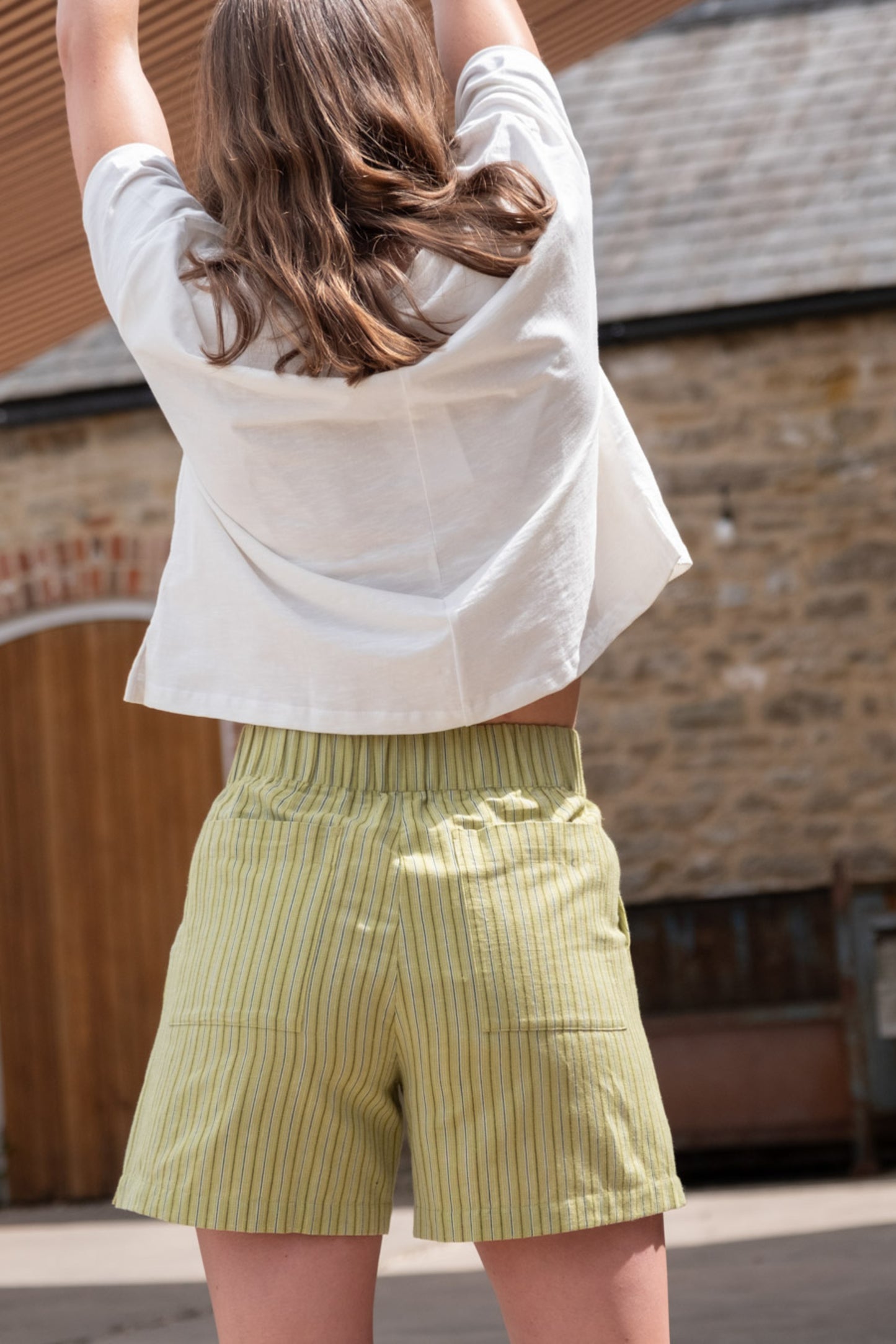 Image of model wearing BIBICO Petra Day Short in Avocado Stripe. Petra Shorts are a pull-on style short in a mid-thigh length. Produced by Fair Trade Certified makers using organic cotton.