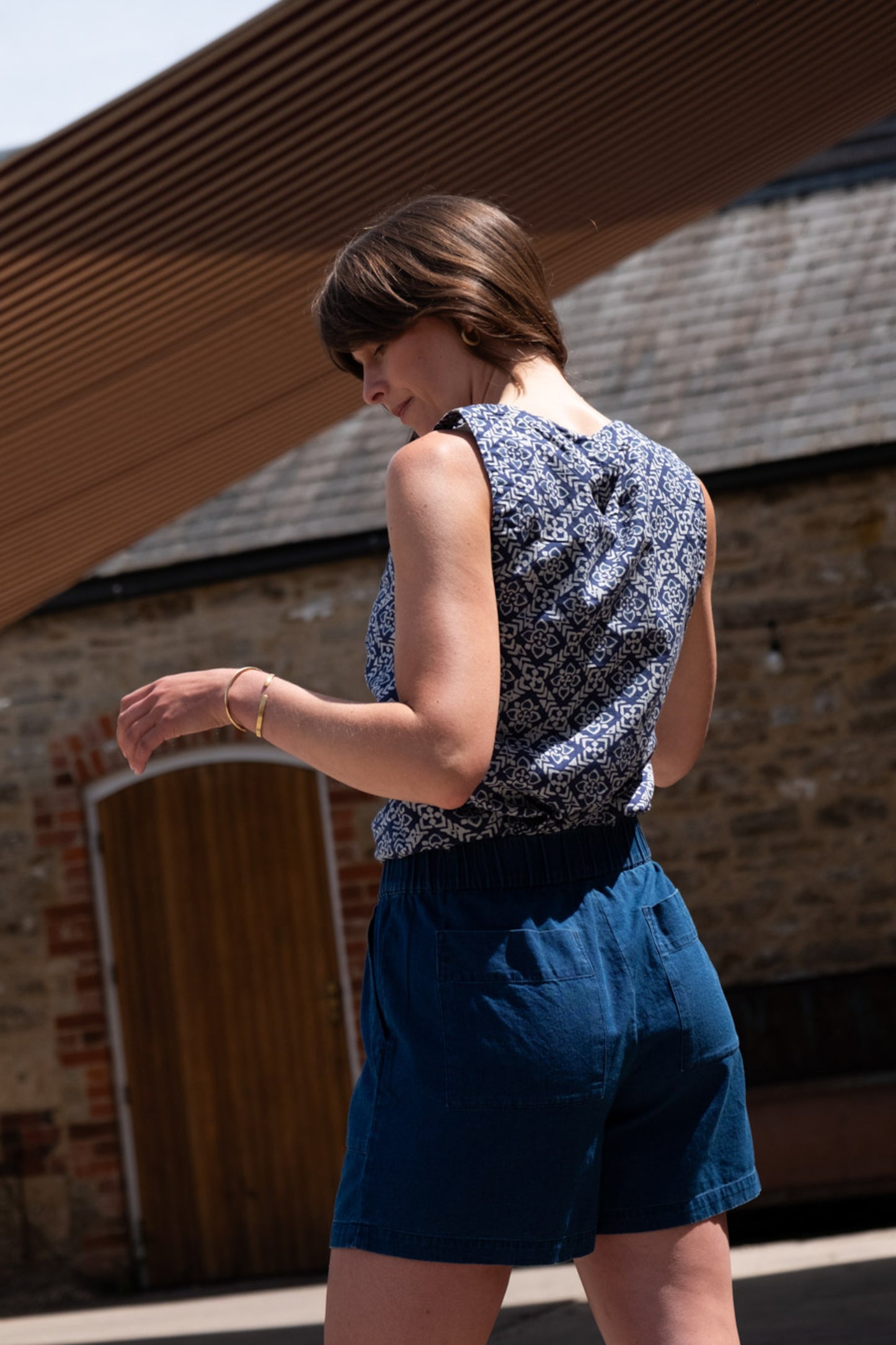 Image of model wearing BIBICO Petra Day Short in Textured Denim. Petra Shorts are a pull-on style short in a mid-thigh length. Produced by Fair Trade Certified makers using organic cotton.