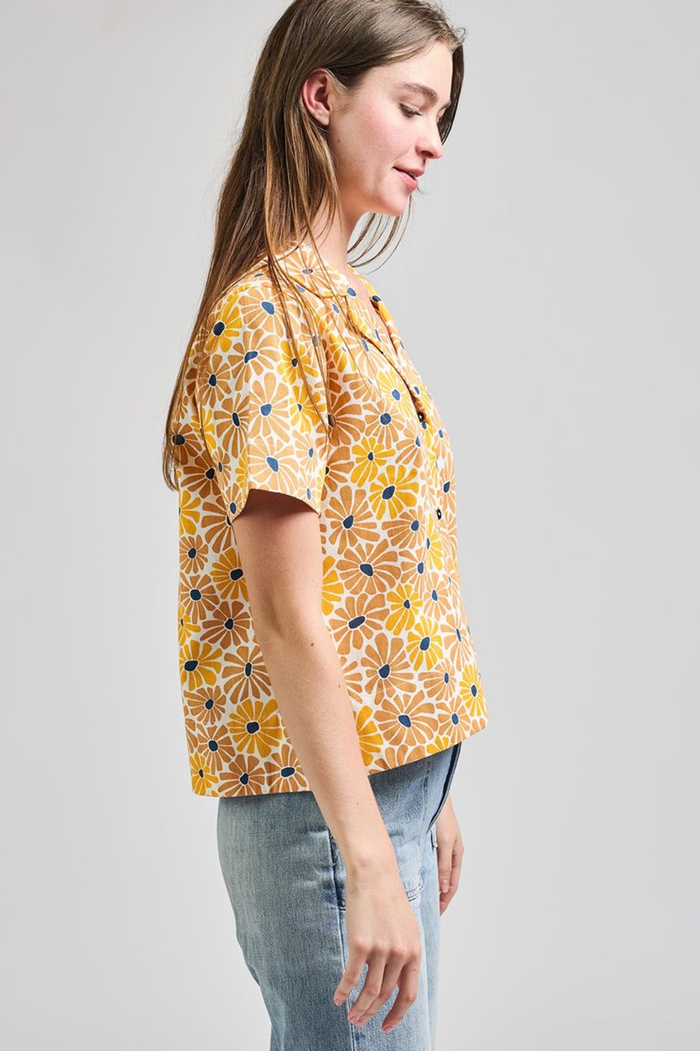 Image of model wearing MATA TRADERS Fair Trade Certified Camp Shirt in Sunny Floral Print. Camp Top is an open neck vintage inspired short sleeve button down. Sunny Floral Print is an orange, yellow, and teal sunflower motif hand block printed on Cotton twill fabric.