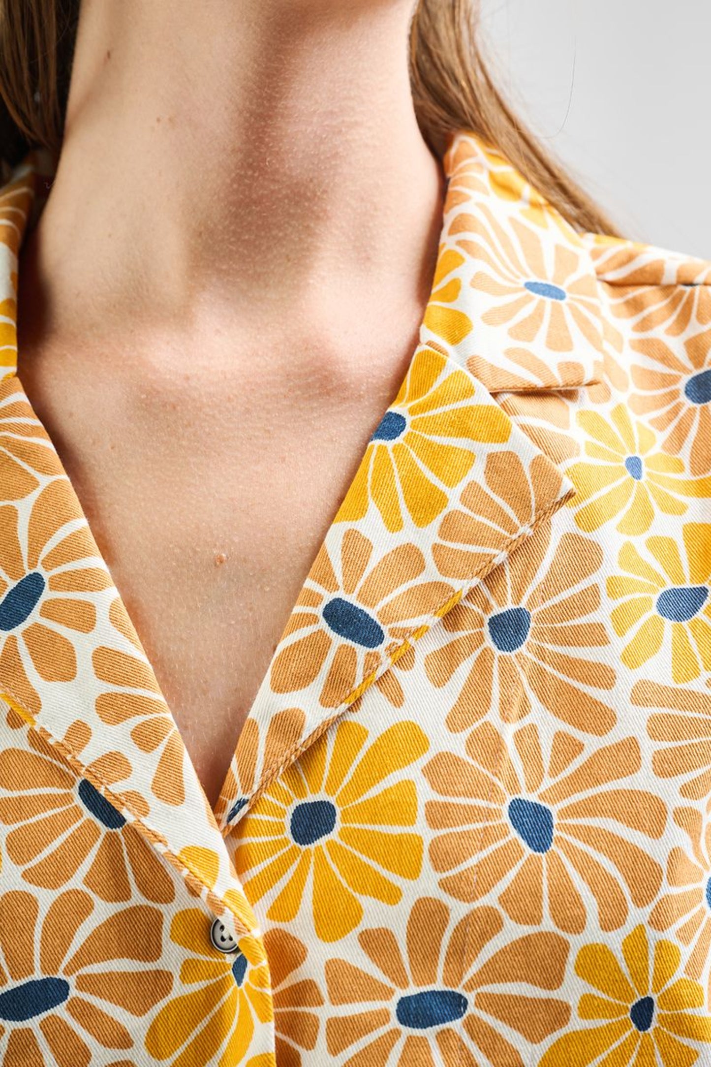 Image of model wearing MATA TRADERS Fair Trade Certified Camp Shirt in Sunny Floral Print. Camp Top is an open neck vintage inspired short sleeve button down. Sunny Floral Print is an orange, yellow, and teal sunflower motif hand block printed on Cotton twill fabric.