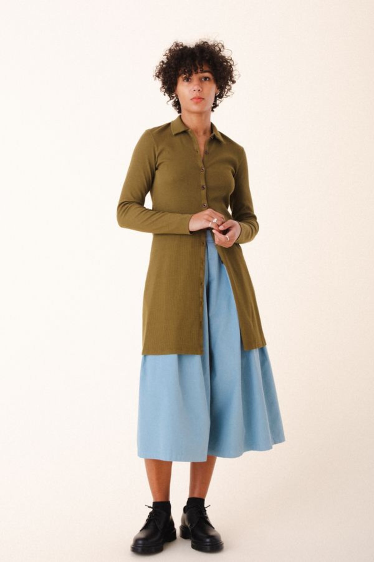Image of model wearing Cavalos Shirt Dress in Herb Green Rib. Cavalos is a fitted shirt dess with a classic collar that hits mid-thigh made from organic cotton Ribbed fabric.