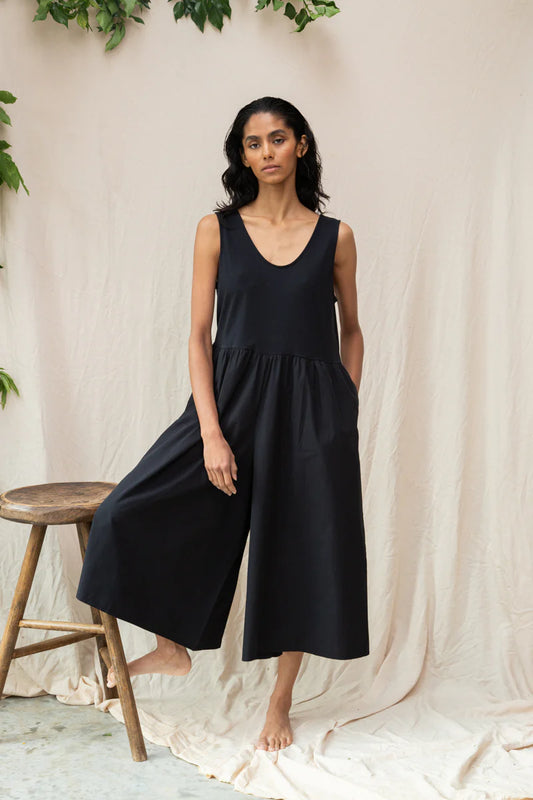 Image of model wearing Beaumont Organic Rory Coton Jumpsuit in black. Rory is a pull on style sleeveless jumpsuit with a scoop neck, relaxed waistline, and wide culotte style leg opening. Cropped fit. Ethically made in Portugal from organic cotton.