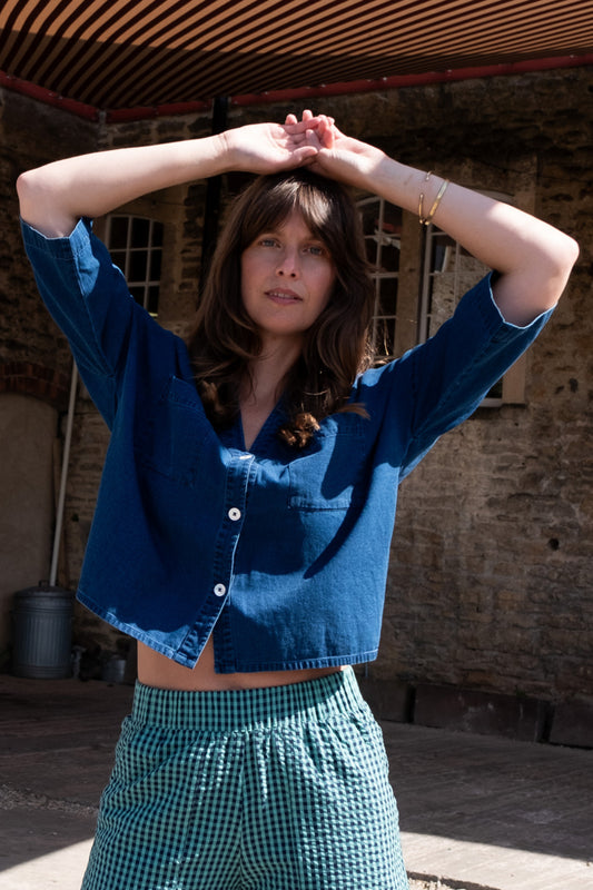 Image of model wearing BIBICO Ava Oversized Button Down in Textured Indigo Denim. Ava is a boxy fitting button down with an open neckline and elbow length sleeve. Produced by Fair Trade Certified makers using organic cotton.  