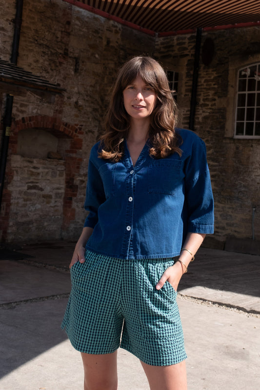 Image of model wearing BIBICO Ava Oversized Button Down in Textured Indigo Denim. Ava is a boxy fitting button down with an open neckline and elbow length sleeve. Produced by Fair Trade Certified makers using organic cotton.  