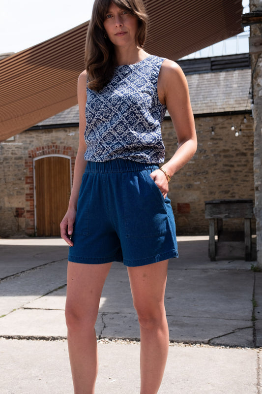 Image of model wearing BIBICO Petra Day Short in Textured Denim. Petra Shorts are a pull-on style short in a mid-thigh length. Produced by Fair Trade Certified makers using organic cotton.