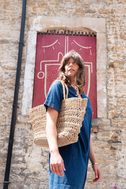 Image of model wearing BIBICO Fair Trade Clothier's Wren Dress in Textured Denim. Wren Dress is an above the knee Length a-line shift dress with an open neckline and patch pockets. Fair Trade Certified production using Indigo dyed organic cotton.