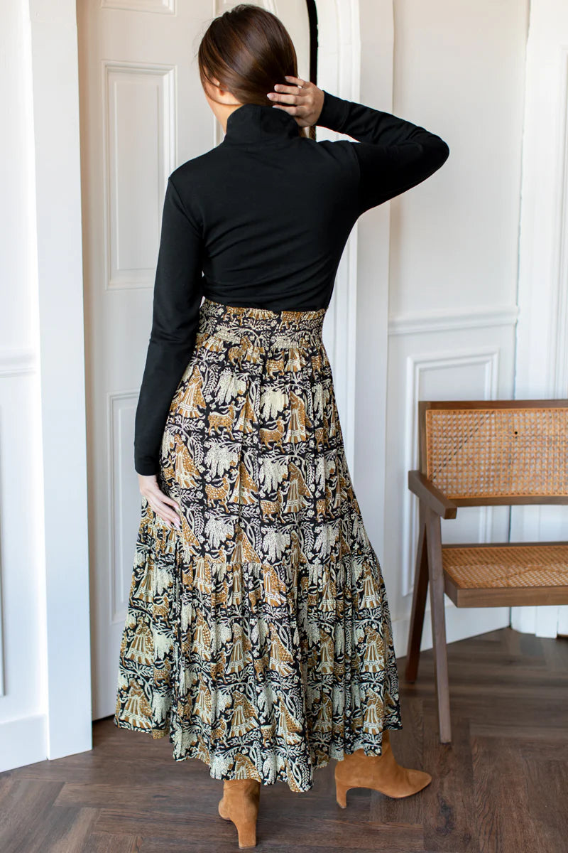 Image of model wearing EMERSON FRY Shirred Maxi Skirt in Story Print Floral. This skirt has a tiered hemline and is hand block printed with a tan and beige floral motif on black modal. 