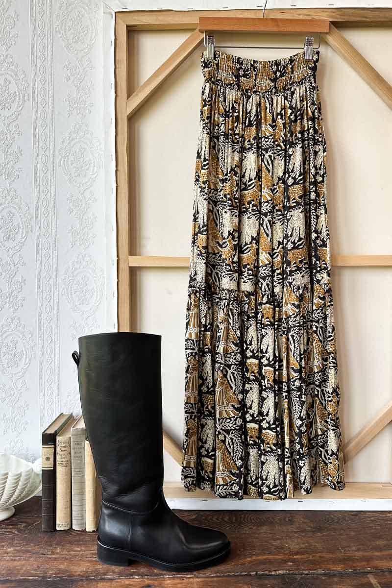 Image of model wearing EMERSON FRY Shirred Maxi Skirt in Story Print Floral. This skirt has a tiered hemline and is hand block printed with a tan and beige floral motif on black modal. 