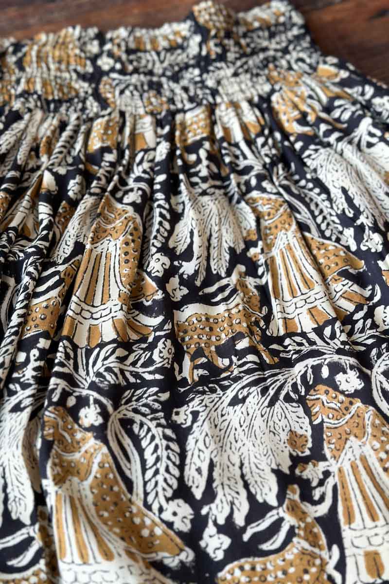 Image of model wearing EMERSON FRY Shirred Maxi Skirt in Story Print Floral. This skirt has a tiered hemline and is hand block printed with a tan and beige floral motif on black modal. 