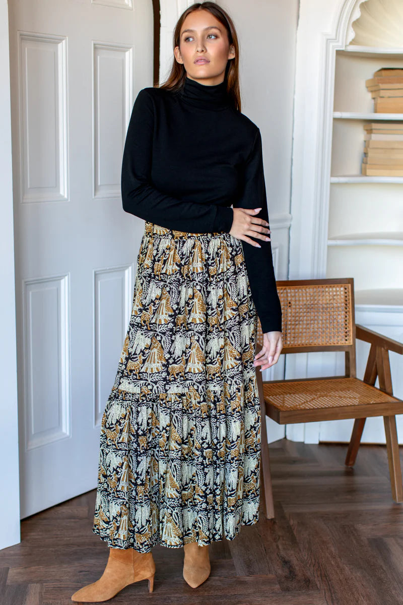Image of model wearing EMERSON FRY Shirred Maxi Skirt in Story Print Floral. This skirt has a tiered hemline and is hand block printed with a tan and beige floral motif on black modal. 