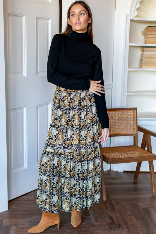 Image of model wearing EMERSON FRY Shirred Maxi Skirt in Story Print Floral. This skirt has a tiered hemline and is hand block printed with a tan and beige floral motif on black modal. 
