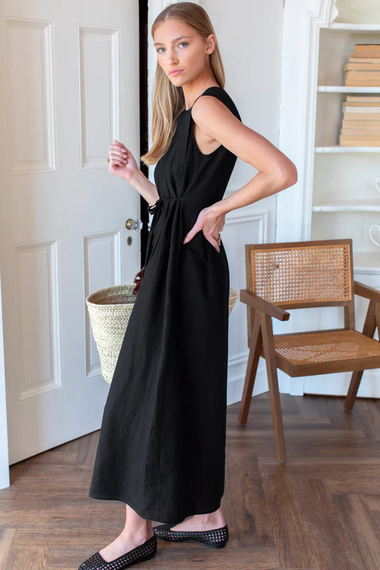 Image of model wearing Emerson Fry Plait Maxi Dress in Black Viscose Linen. Plait Dress is a sleeveless summer dress with front pleat details on the body, cinched waistline, and a-line style maxi skirt.