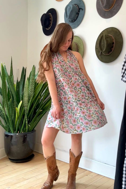 Image of model wearing MAELU DESIGNS Poppy Mini Dress in Cici Print. Poppy is a sleeveless cotton sundress that hits about the knee with an a-line, tiered body and ruffled collar. Offered in a block printed Cotton featuring an all over purple, teal, and yellow floral print. 