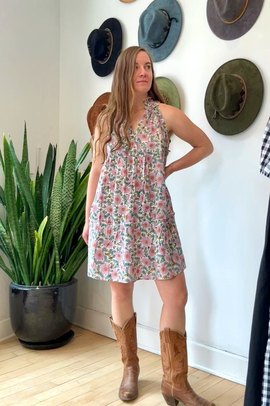 Image of model wearing MAELU DESIGNS Poppy Mini Dress in Cici Print. Poppy is a sleeveless cotton sundress that hits about the knee with an a-line, tiered body and ruffled collar. Offered in a block printed Cotton featuring an all over purple, teal, and yellow floral print. 