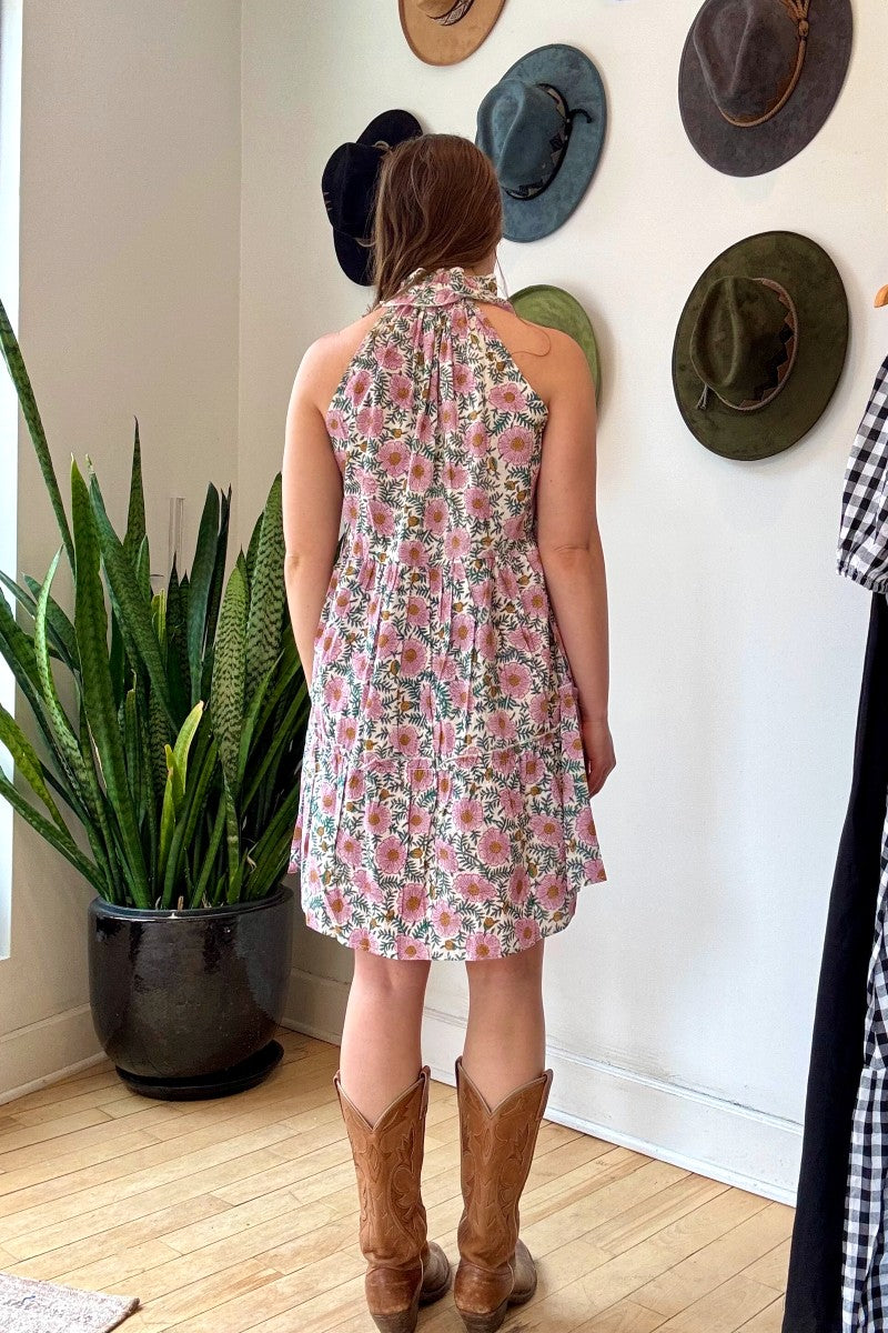 Image of model wearing MAELU DESIGNS Poppy Mini Dress in Cici Print. Poppy is a sleeveless cotton sundress that hits about the knee with an a-line, tiered body and ruffled collar. Offered in a block printed Cotton featuring an all over purple, teal, and yellow floral print. 