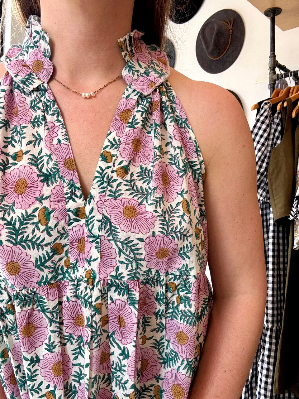 Image of model wearing MAELU DESIGNS Poppy Mini Dress in Cici Print. Poppy is a sleeveless cotton sundress that hits about the knee with an a-line, tiered body and ruffled collar. Offered in a block printed Cotton featuring an all over purple, teal, and yellow floral print. 