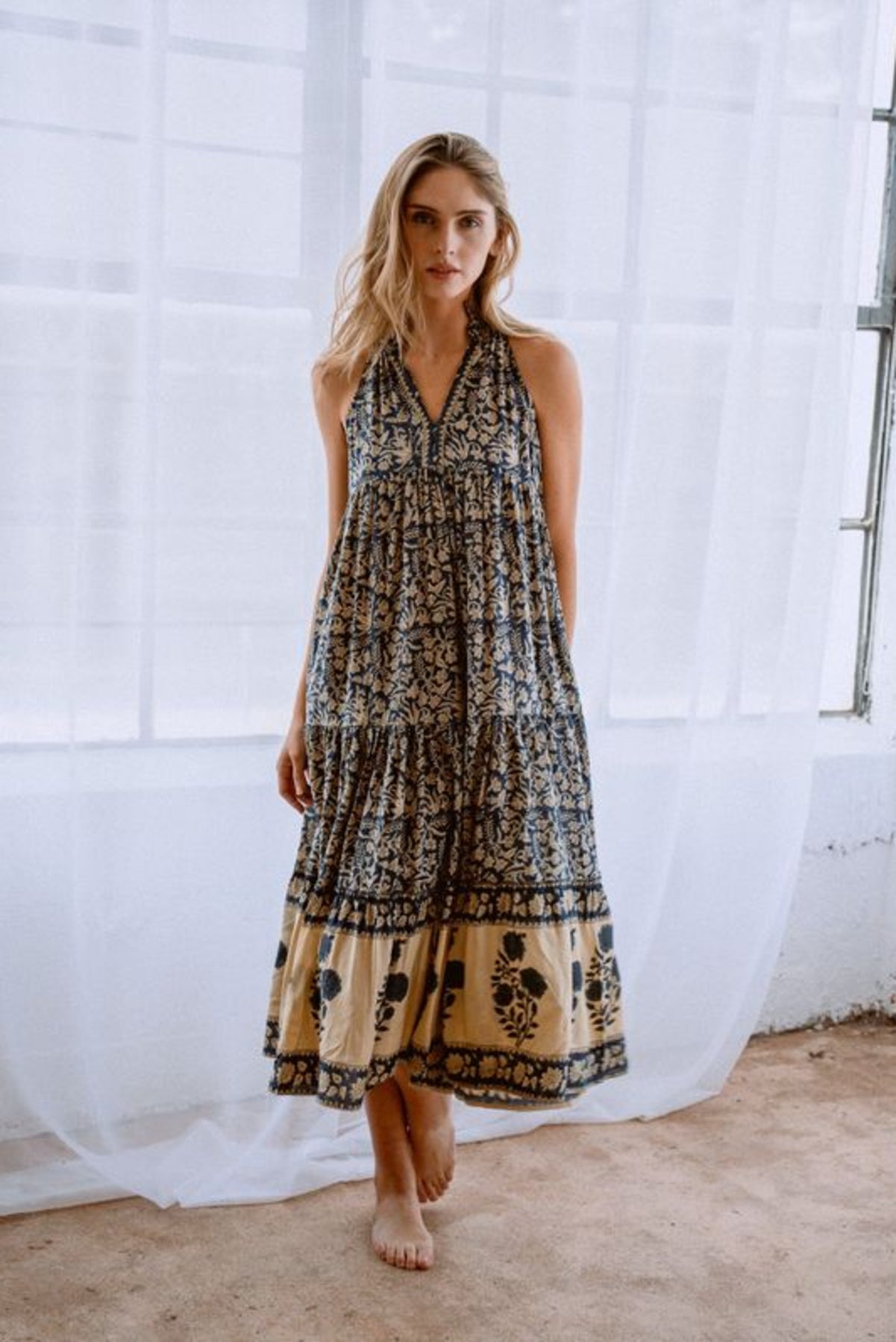 Image of model wearing MAELU DESIGNS Poppy Tiered Sundress. Poppy dress is a halter style sundress with flowing, tiered a line skirt, v-neck opening, and frilled bodice in a hand block printed Delia Floral Printed Modal. 