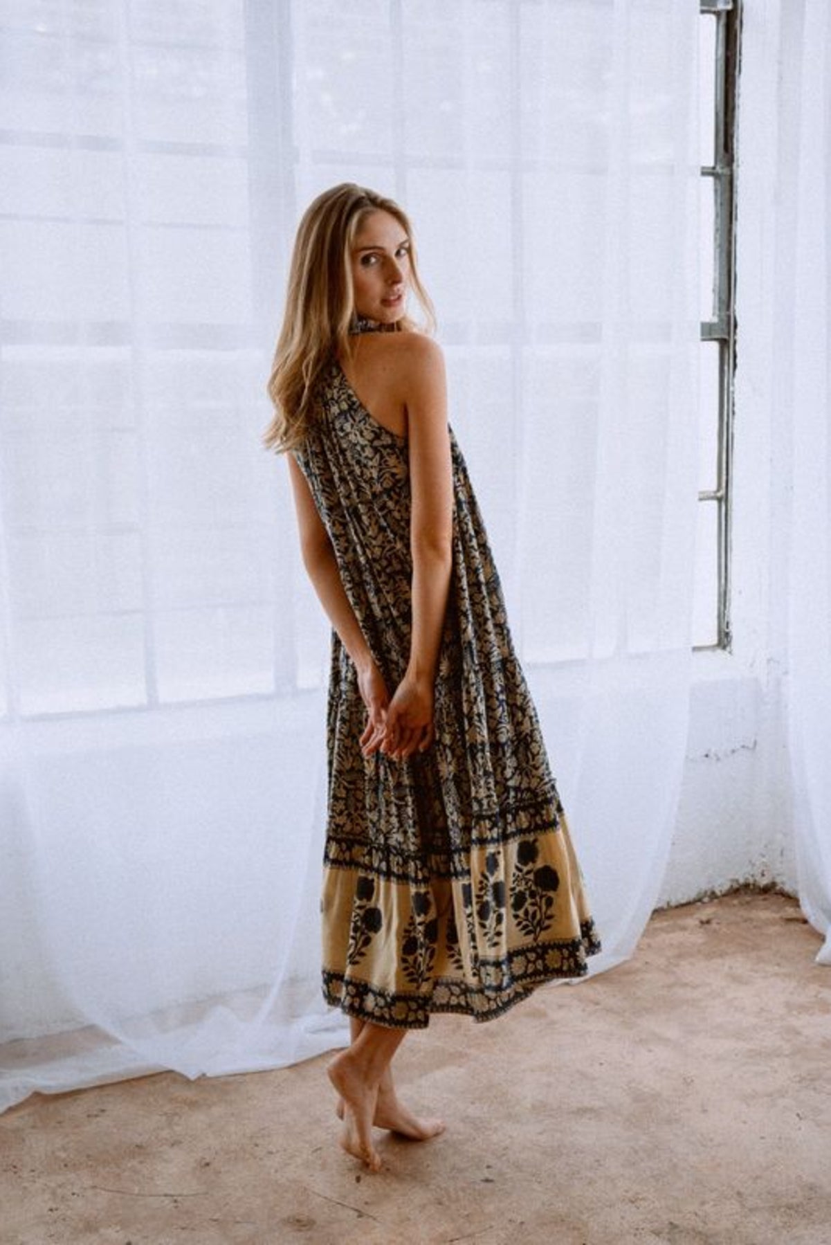 Image of model wearing MAELU DESIGNS Poppy Tiered Sundress. Poppy dress is a halter style sundress with flowing, tiered a line skirt, v-neck opening, and frilled bodice in a hand block printed Delia Floral Printed Modal. 