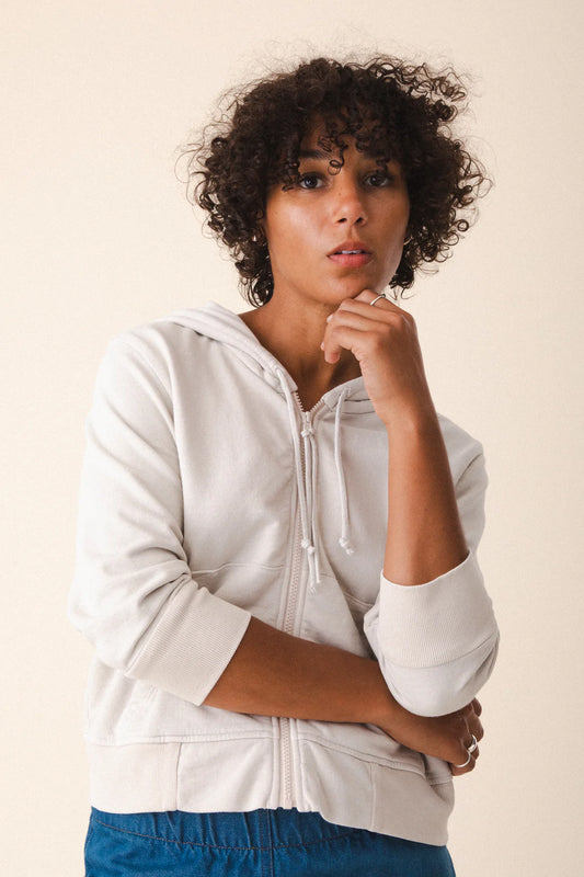 Image of model wearing Prairie Underground Simple Life Hoodie in Oyster White. Simple Life is a slightly cropped zip front hoodie sweatshirt made from an organic cotton fleece. Designed and produced in Seattle, Washington.