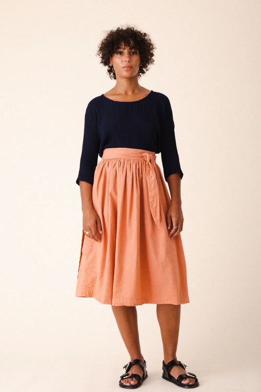 Image of model wearing Prairie Underground Interval Wrap Skirt in Cedar Chest. Interval Skirt is a true wrap skirt that hits below the knee with a sash tie, made in Seattle, Washington from a Cedar Pink organic cotton muslin.