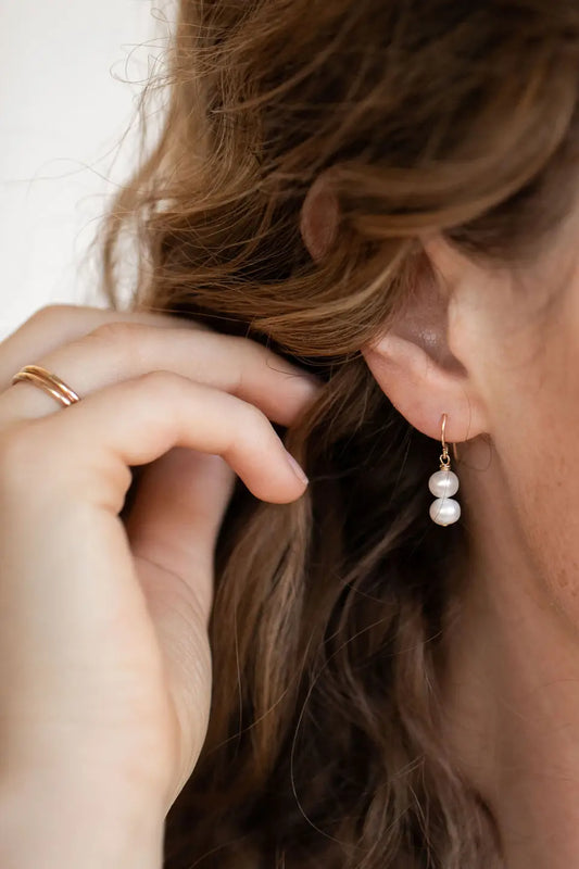 Image of Sheena Marshall Jewelry handmade Pearl Drop Earring on model - dual pearl pendant on pull through 14k goldfill hook earring. Simple, luxurious jewelry handmade in Denver, Colorado.