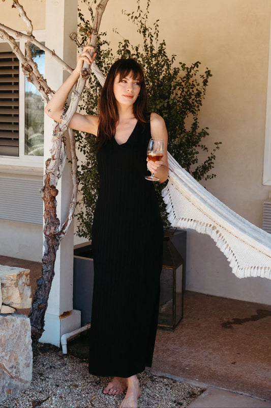 Image of model wearing Whimsy + Row Ava Reversible Column Dress in Black Eco-Rib. Ava Dress has a v-neck or high neck open and can be worn front to back. Full length with symmetrical side slits at hem. Sleeveless. Made in Los Angeles.