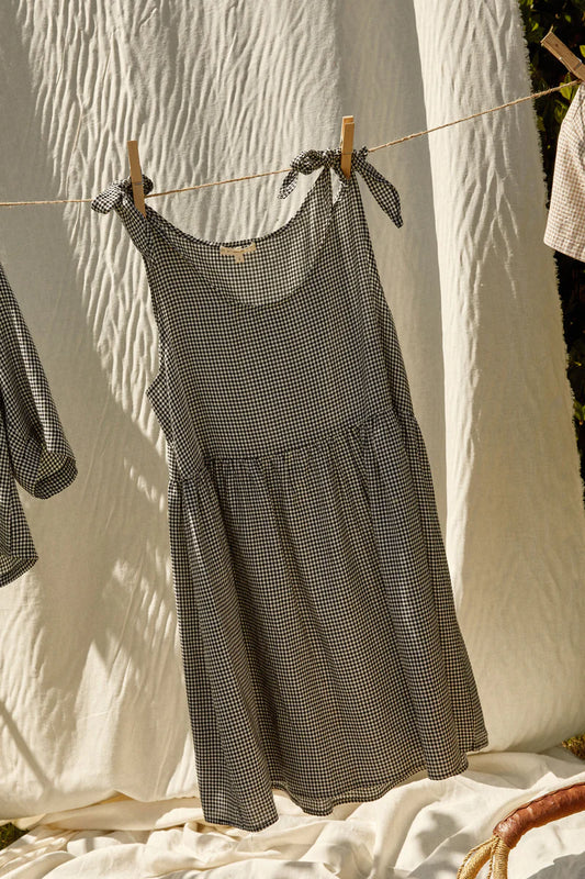 Image of WHIMSY AND ROW KATE MINI SUNDRESS IN BLACK AND WHITE GINGHAM. Kate Dress is a loose fitting mini dress with adjustable tie shoulder straps. Made in USA from black + white gingham TENCEL fabric.